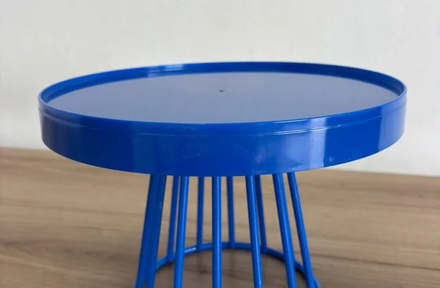 Boleira de metal azul royal, com tampo redondo de borda alta e base vazada de hastes, sobre uma bancada de madeira