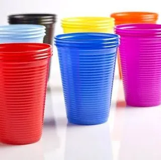 Copos plásticos descartáveis em vermelho, azul, amarelo, rosa, verde, preto e laranja, agrupados sobre fundo branco